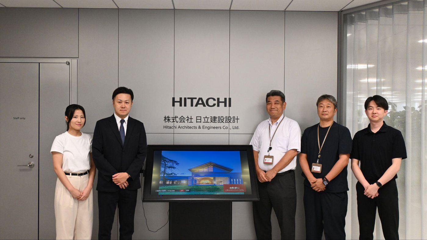 MediaSpaceコンシェルジュを設置した株式会社日立建設設計様のエントランスと、導入に携わった関係者の集合写真